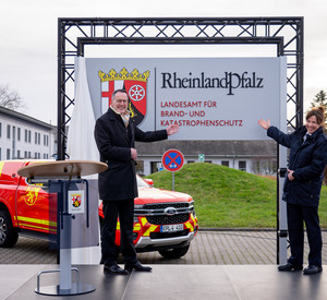 Innenminister Michael Ebling und Landesbrand- und Katastrophenschutzinspekteurin Kirstin Eisenhauer mit dem Schild der neuen Behörde. Im Hintergrund stehen landeseigene Einsatzfahrzeuge im neu gestalteten Design.