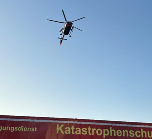 Ein Polizei-Hubschrauber fliegt über einem Einsatzfahrzeug des Katastrophenschutzes.